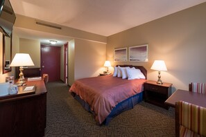 Habitación de hotel con cama, dos mesitas de noche con lámparas, escritorio, silla y puerta que da a otra habitación.