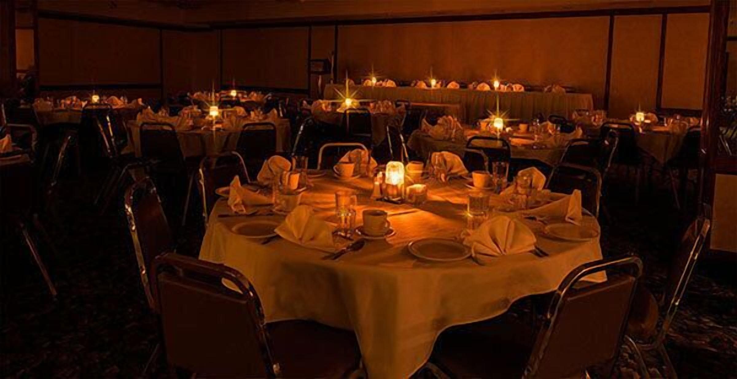 Een feestzaal met ronde tafels gedekt voor een diner, elk met kaarsen en servies.