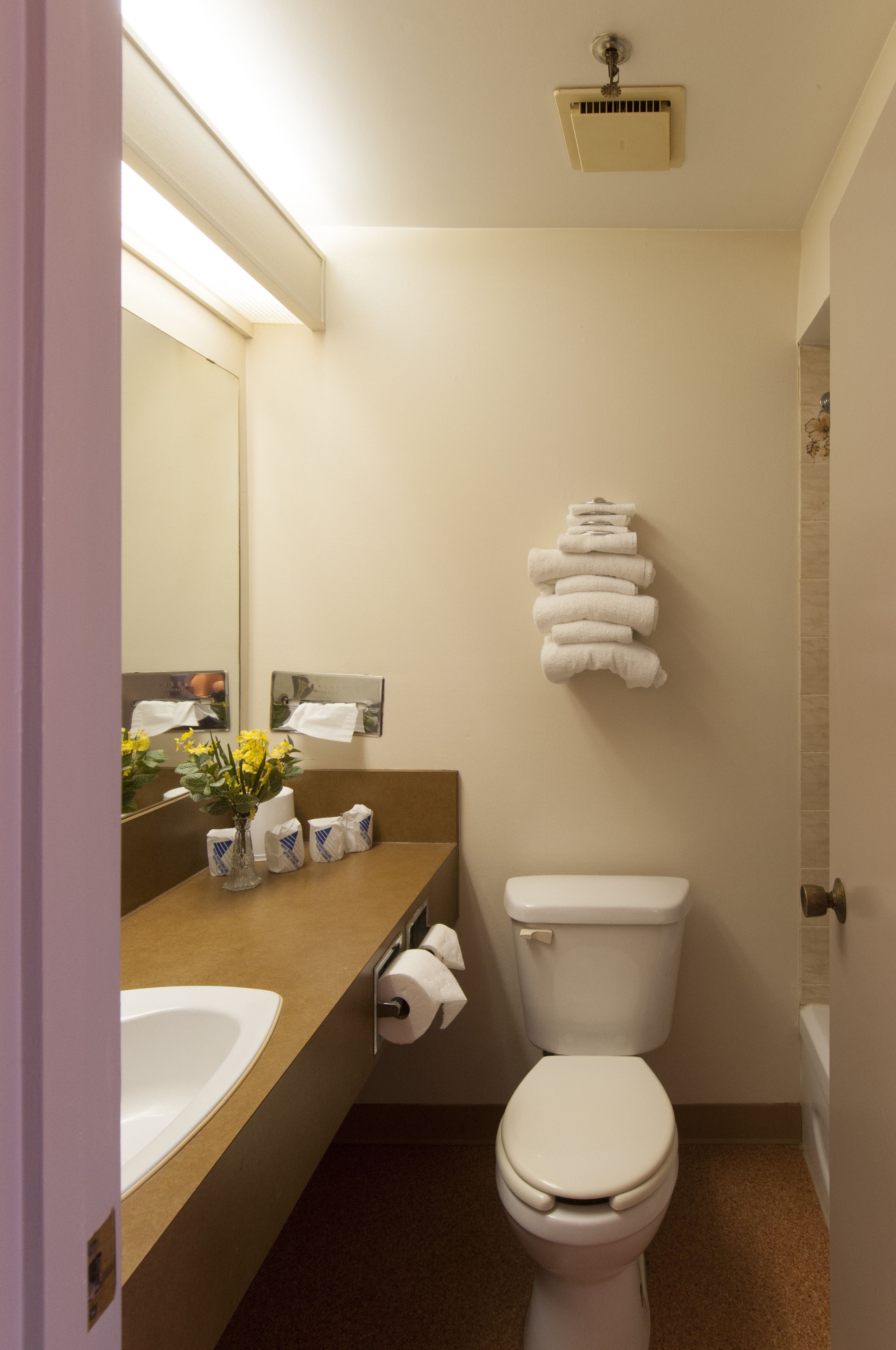 A small bathroom with a toilet, sink, and mirror. There are towels and toiletries on the counter.