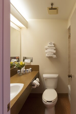 Un baño pequeño con inodoro, lavamanos y espejo. Hay toallas y artículos de aseo en la encimera.