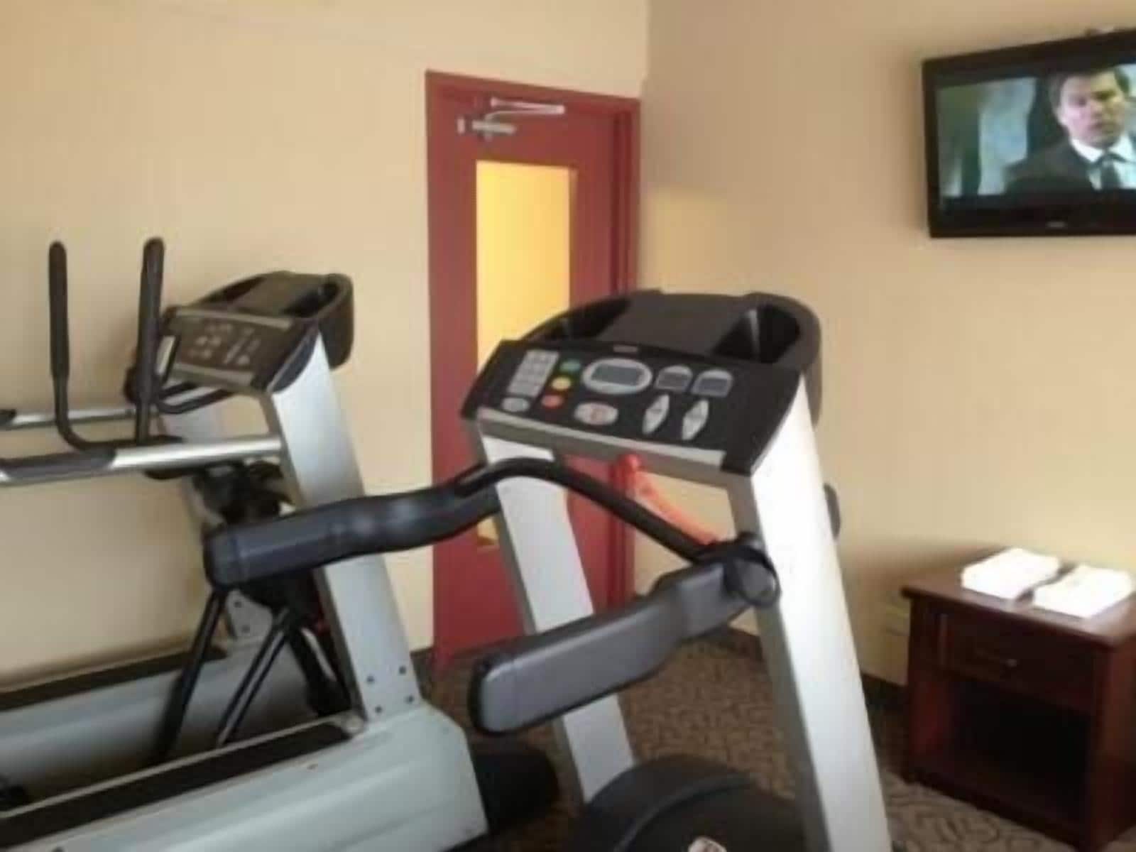 A hotel room with a treadmill, a television, and a small wooden side table.