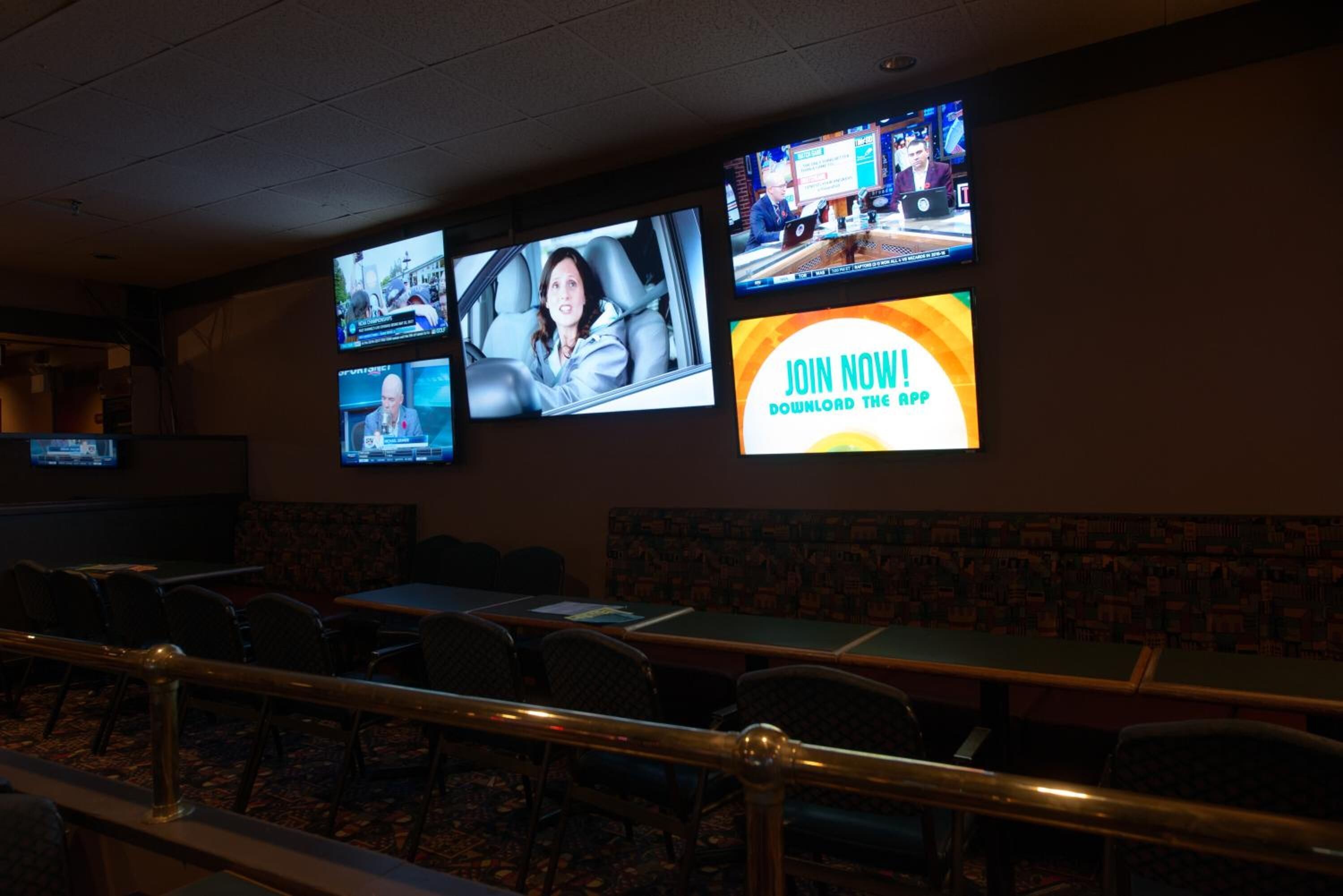 A conference room with multiple screens displaying news and a promotional banner.