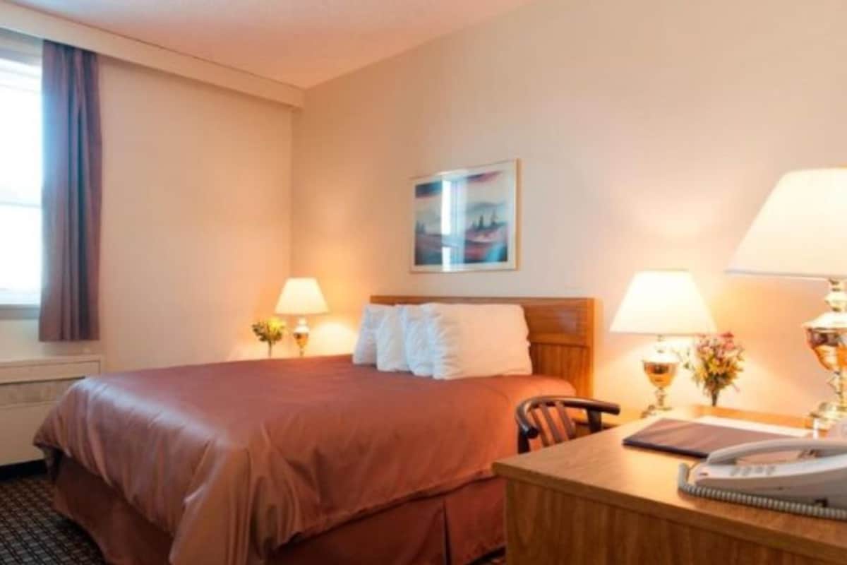 A hotel room with a bed, two bedside lamps, a desk with a telephone, and a window with curtains.