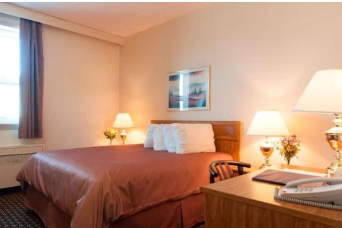 A hotel room with a bed, two bedside lamps, a desk with a telephone, and a window with curtains.