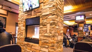 A restaurant with stone walls, a fireplace, and multiple TVs. - Curtis Gordon Motor Hotel (Winnipeg)