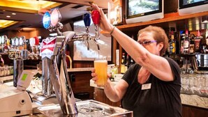 A bar area with multiple beer taps, a person pouring a beer, and a television screen displaying a landscape. - Curtis Gordon Motor Hotel (Winnipeg)