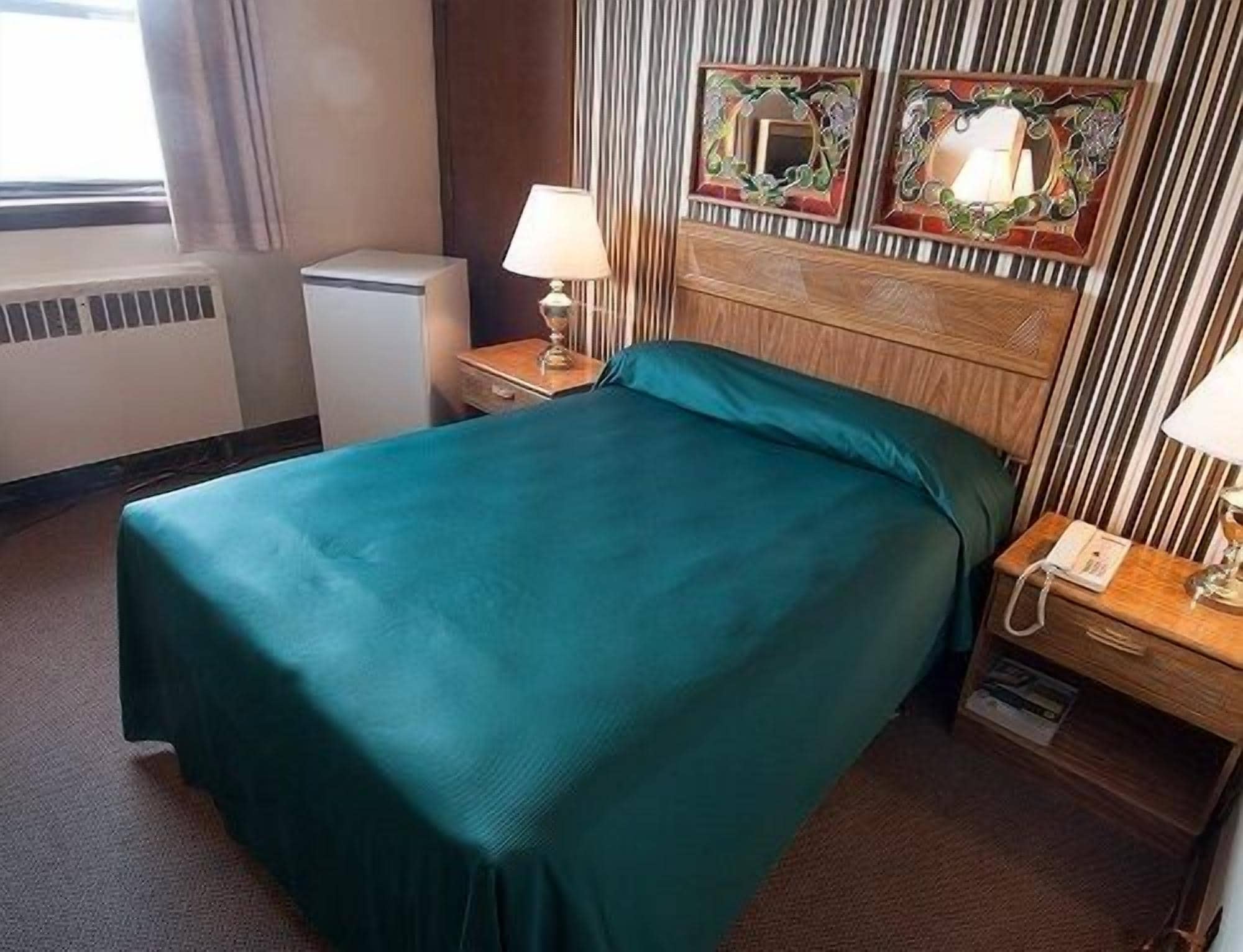 A hotel room with a large bed, a bedside table with a lamp, a small heater, and two decorative mirrors on the headboard.