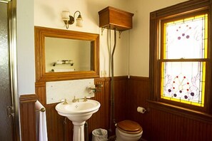 A bathroom with a wooden vanity, a pedestal sink, a toilet, and a stained glass window. - Fordham House (Greenport)