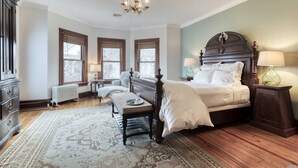 A bedroom with a large bed, a wooden floor, a chandelier, and a window with a view. - Fordham House (Greenport)