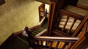 A wooden staircase with a patterned carpet and a view of a room with a patterned wall. - Fordham House (Greenport)