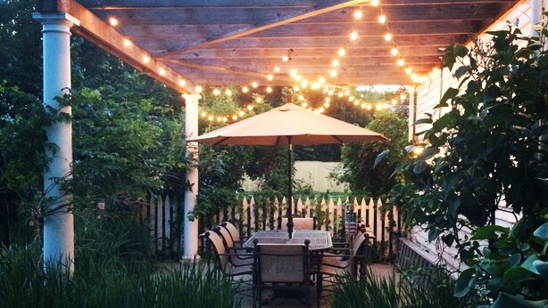 An outdoor patio with a pergola, string lights, and a table with chairs. - Fordham House (Greenport)