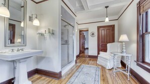 A bathroom with a large mirror, a pedestal sink, and a wooden floor. - Fordham House (Greenport)
