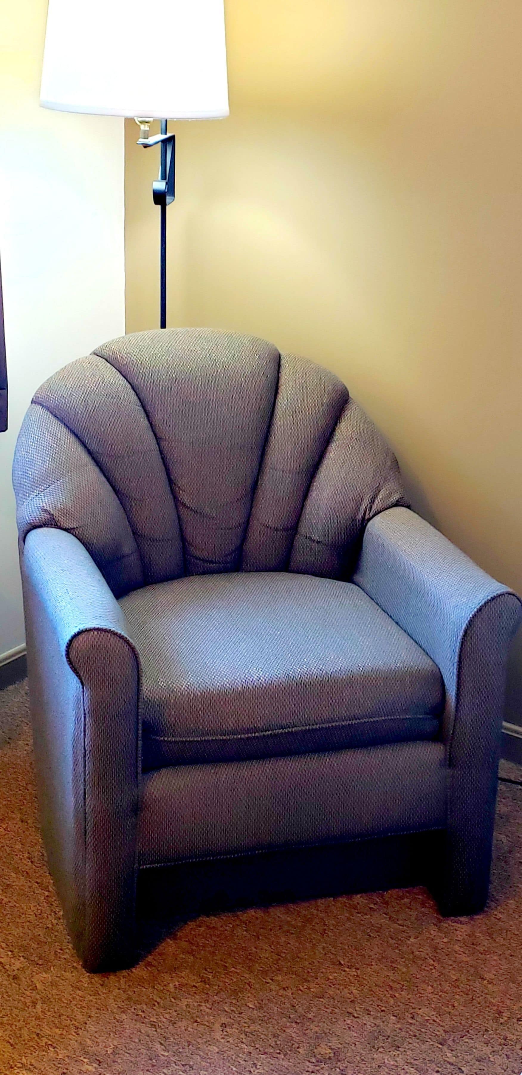 A dark-colored armchair with a high backrest and armrests, positioned on a carpeted floor.