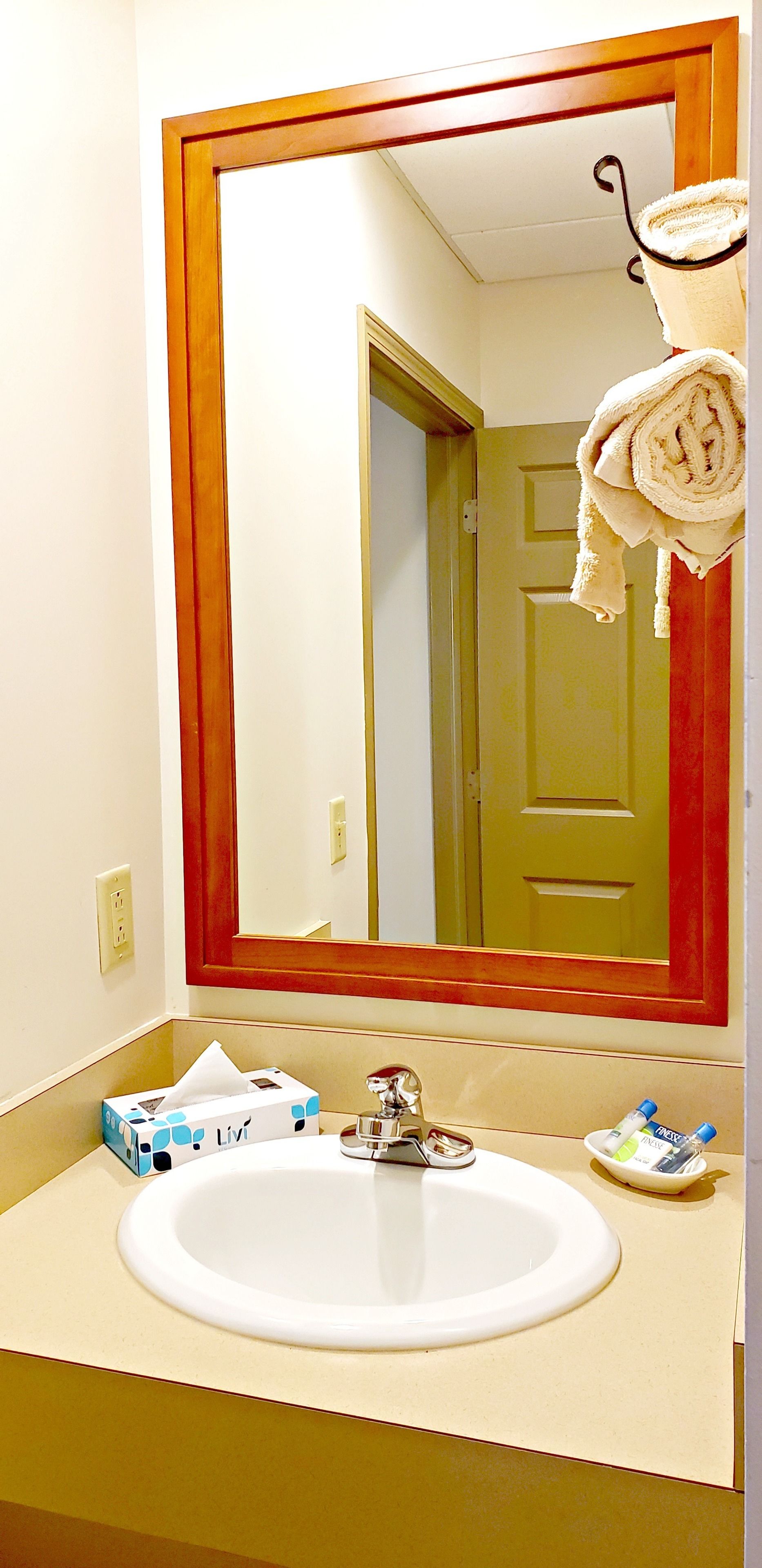 A bathroom with a large mirror, a sink, toiletries, and a towel rack.