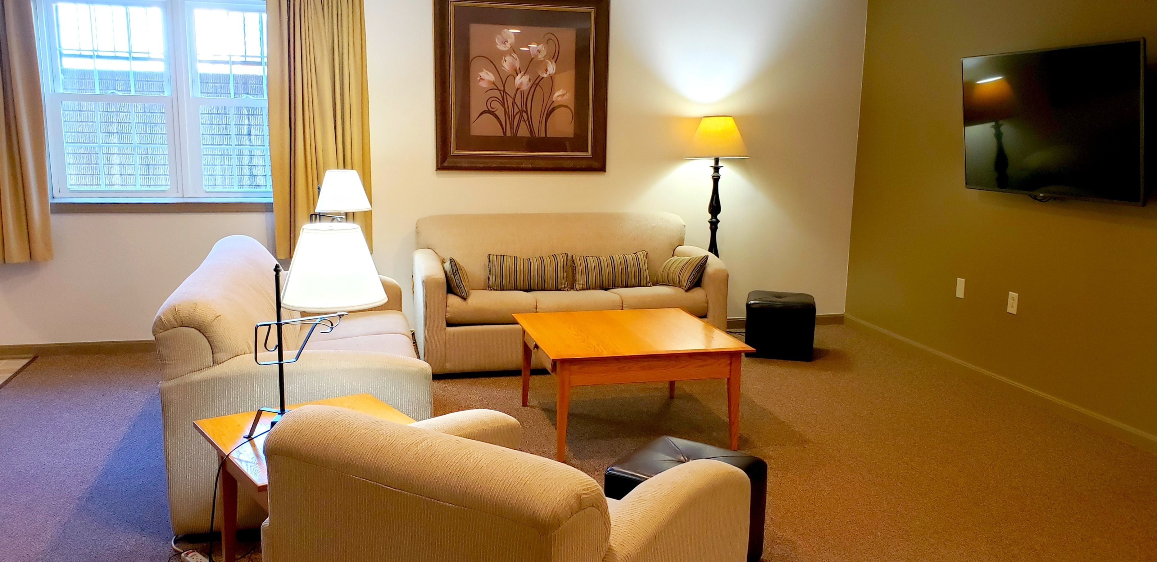 Una sala de estar con sofá, sillones, una mesita de centro, lámpara, televisor y ventana con cortinas.
