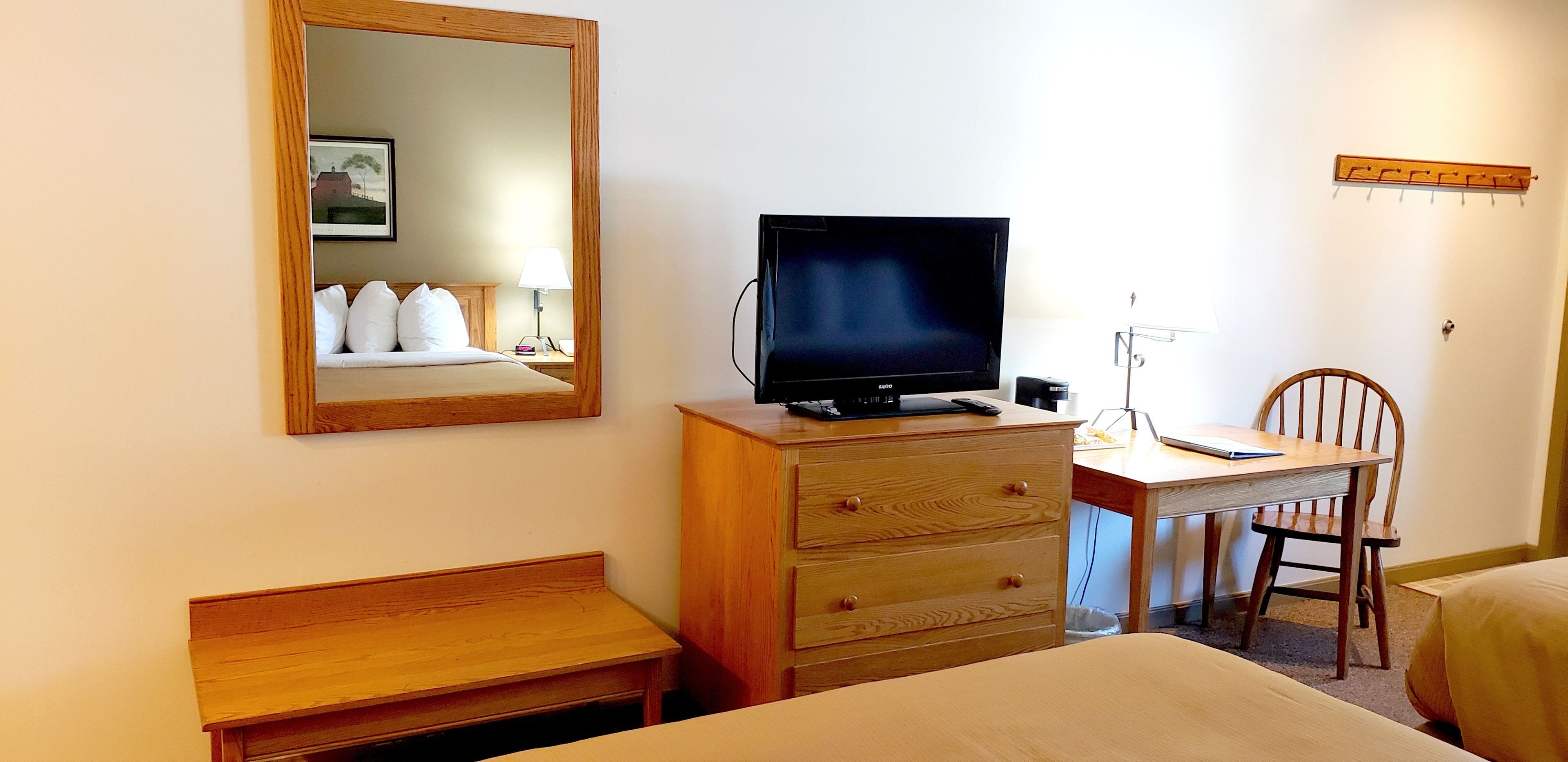 Una habitación de hotel con cama, escritorio de madera, silla, televisor y espejo.