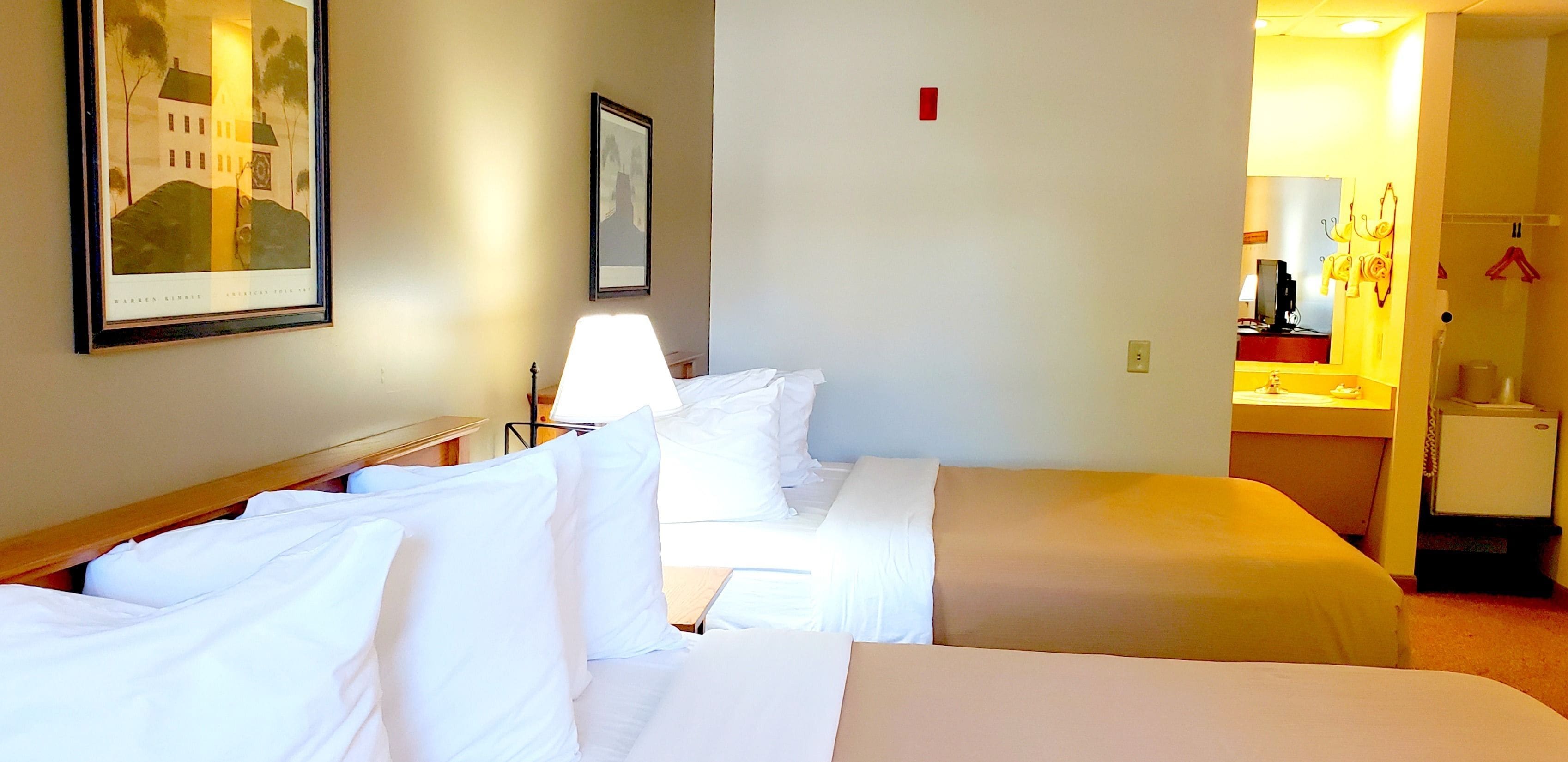 A hotel room with two beds, a desk, a lamp, a mirror, and a framed picture on the wall.