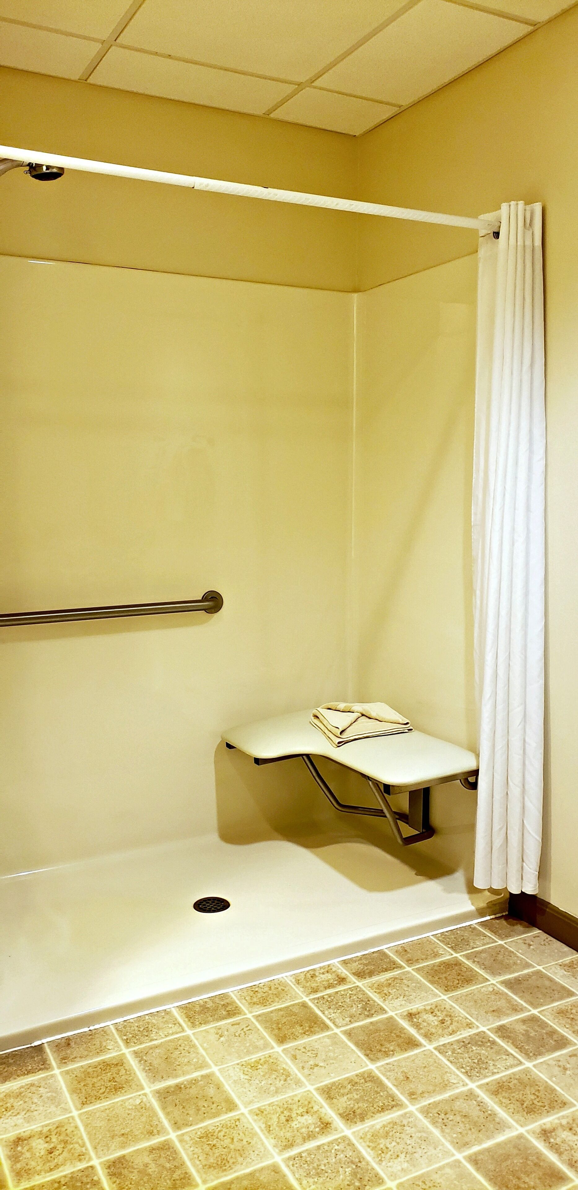 A small, enclosed shower area with a bench, a handrail, and a curtain.
