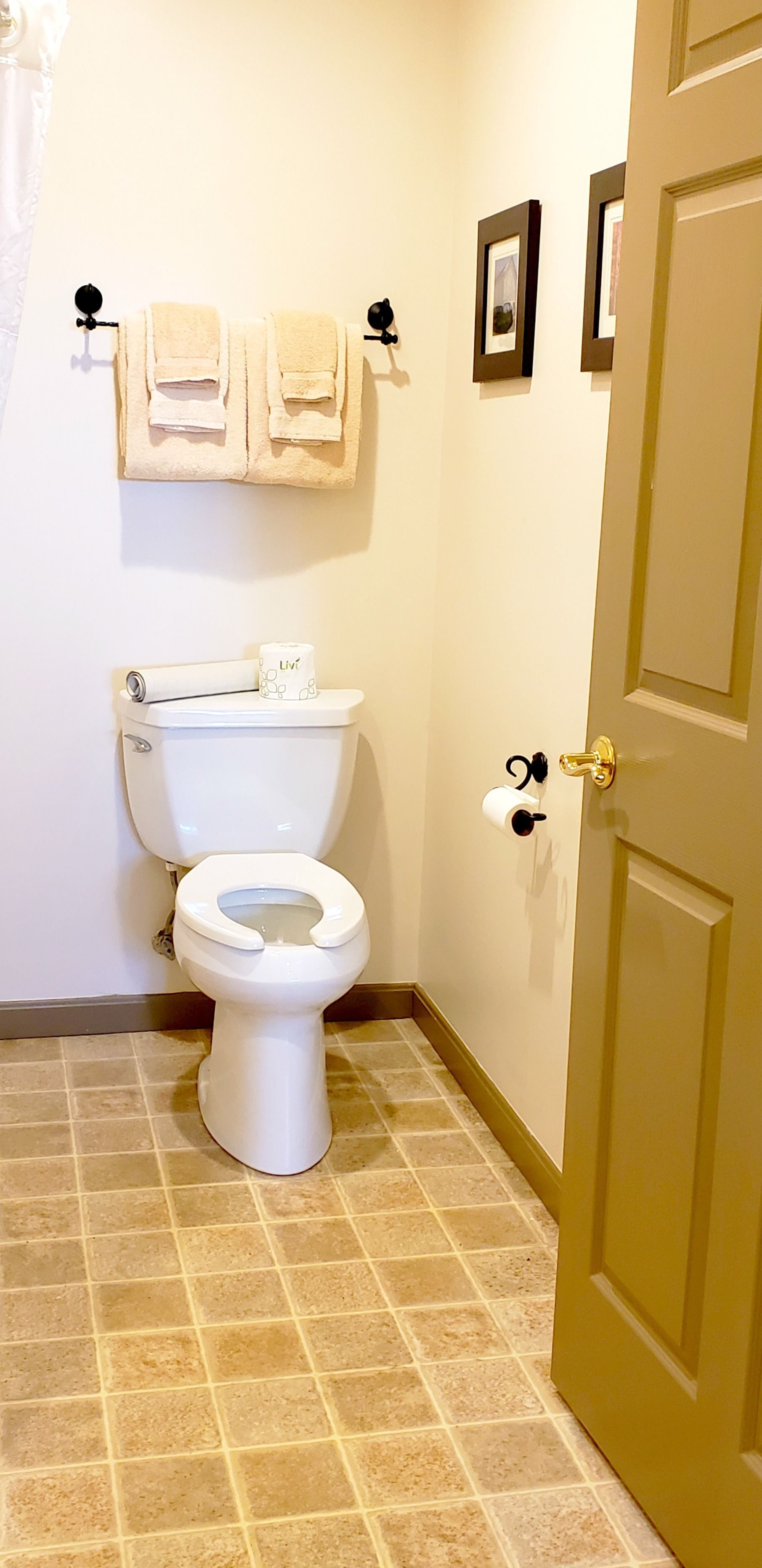 A bathroom with a toilet, a towel rack with towels, a toilet paper holder, and a door.