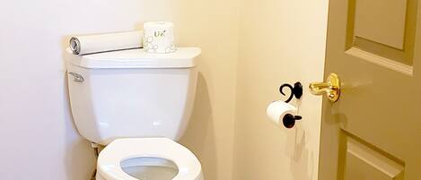 A bathroom with a toilet, a towel rack with towels, a toilet paper holder, and a door.