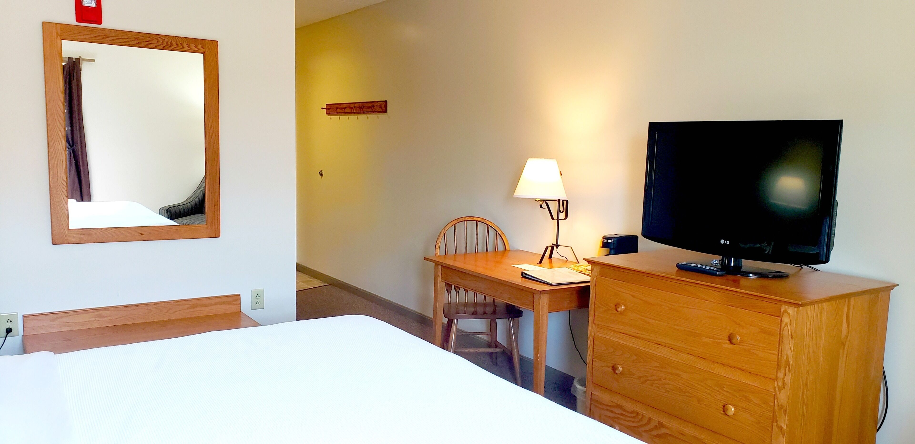Una habitación de hotel con una cama, un escritorio de madera con una silla, un televisor y una lámpara.