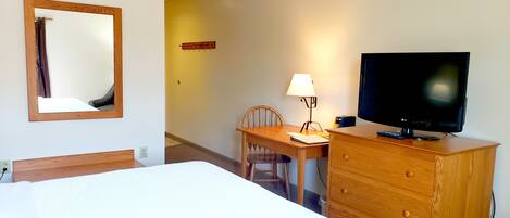 Una habitación de hotel con una cama, un escritorio de madera con una silla, un televisor y una lámpara.