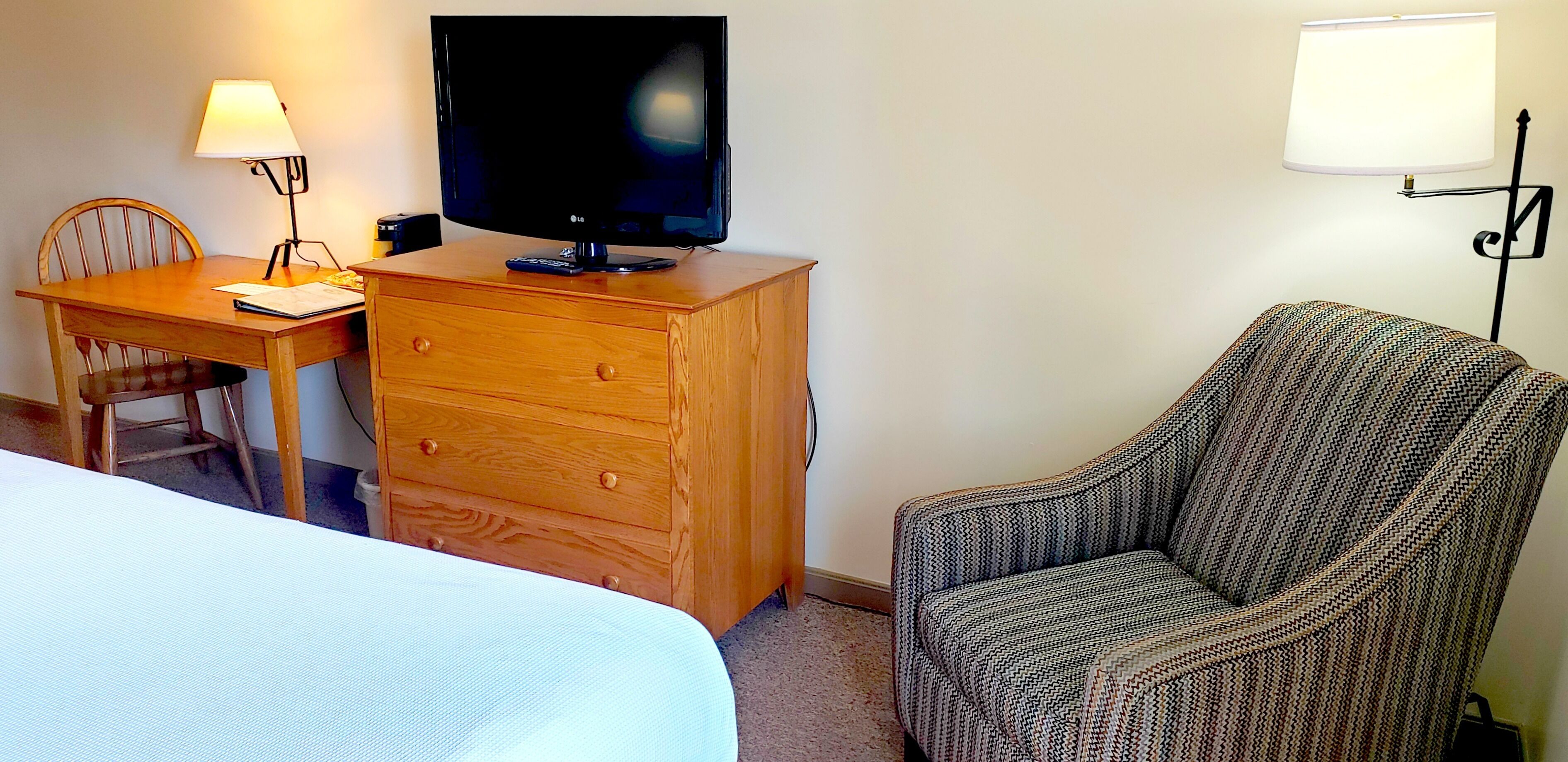 Une chambre d’hôtel avec un bureau en bois, une télévision, une chaise et un lit.