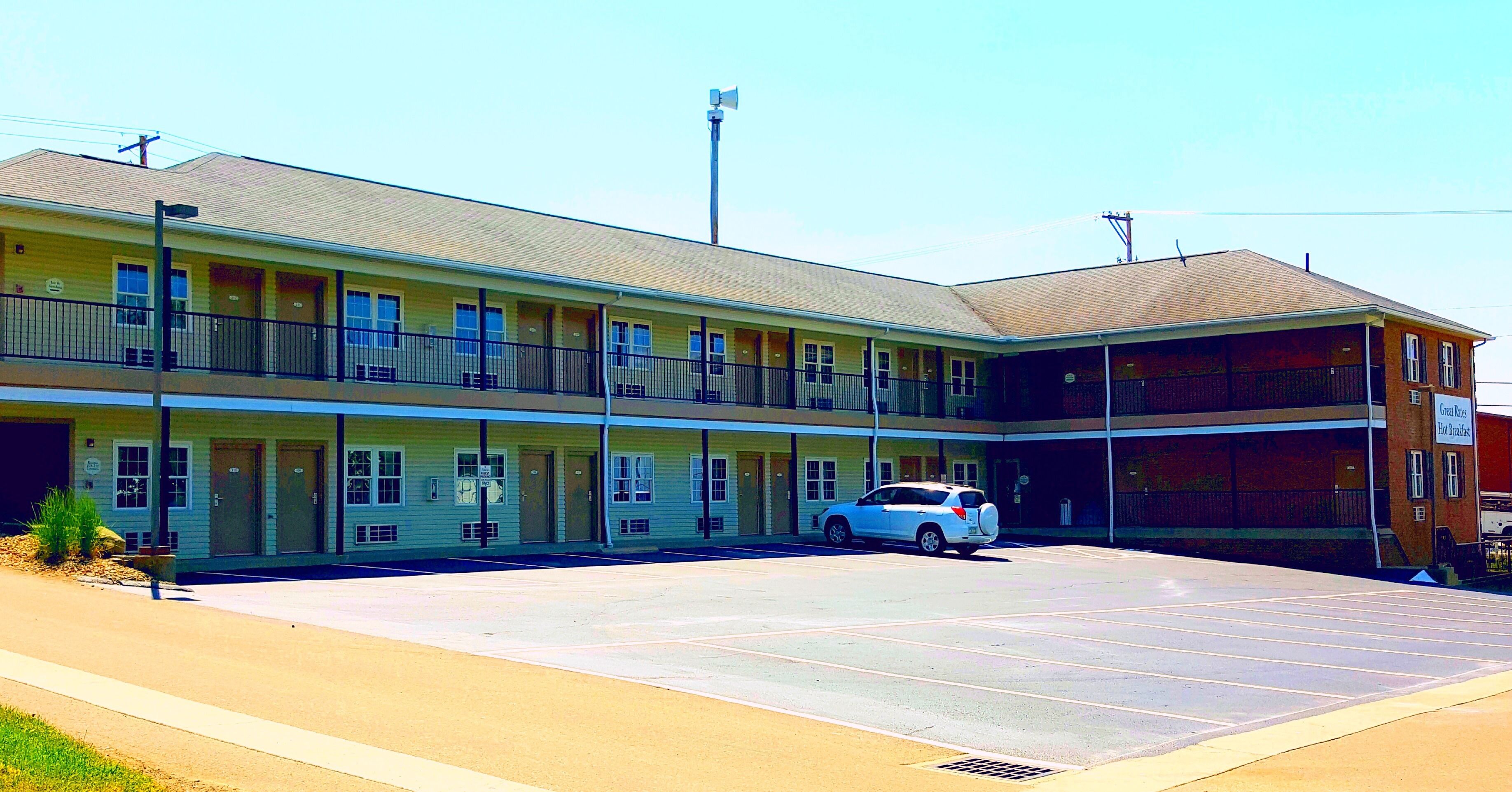 A motel with a two-story structure, a parking lot, and a single white car parked in front.