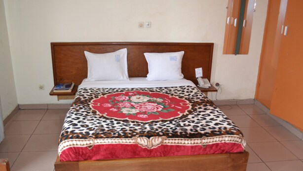 A bed with a floral bedspread, a wooden headboard, and a bedside table with a phone and a book. - Hôtel Lumière Joss (Douala)