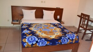 Una cama con una colcha estampada, un cabecero de madera, dos almohadas blancas, una mesita de noche con un libro y una silla.