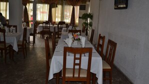 Un comedor con mesas listas para el servicio, sillas de madera y una planta en maceta.