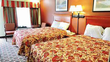 A hotel room with two beds, a chair, a table, and a lamp.