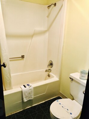 A bathroom with a bathtub, toilet, and a towel rack. - Greystone Motel (Hillsboro)