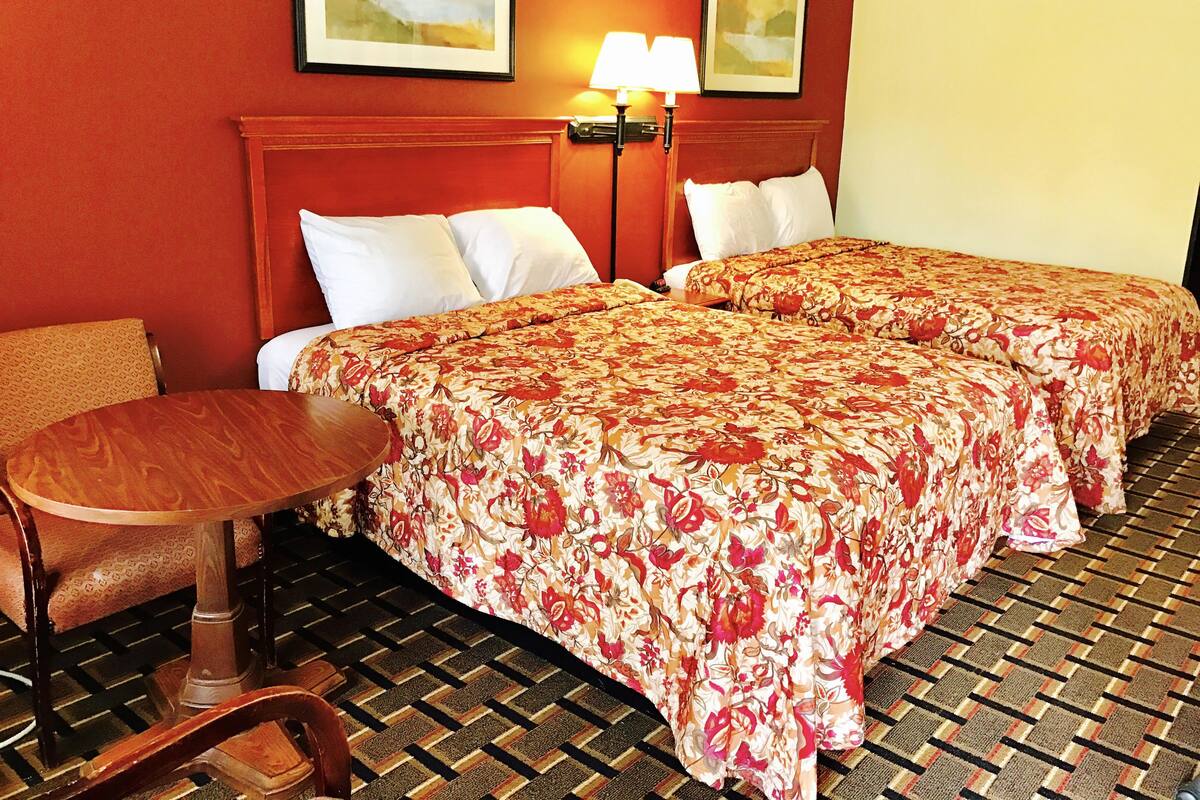 A hotel room with two beds, a wooden chair, a small table, and a patterned floor.