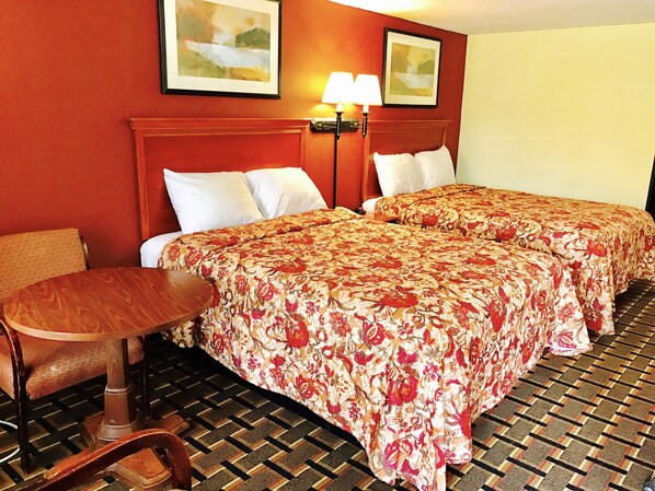 A hotel room with two beds, a wooden chair, a small table, and a patterned floor. - Greystone Motel (Hillsboro)