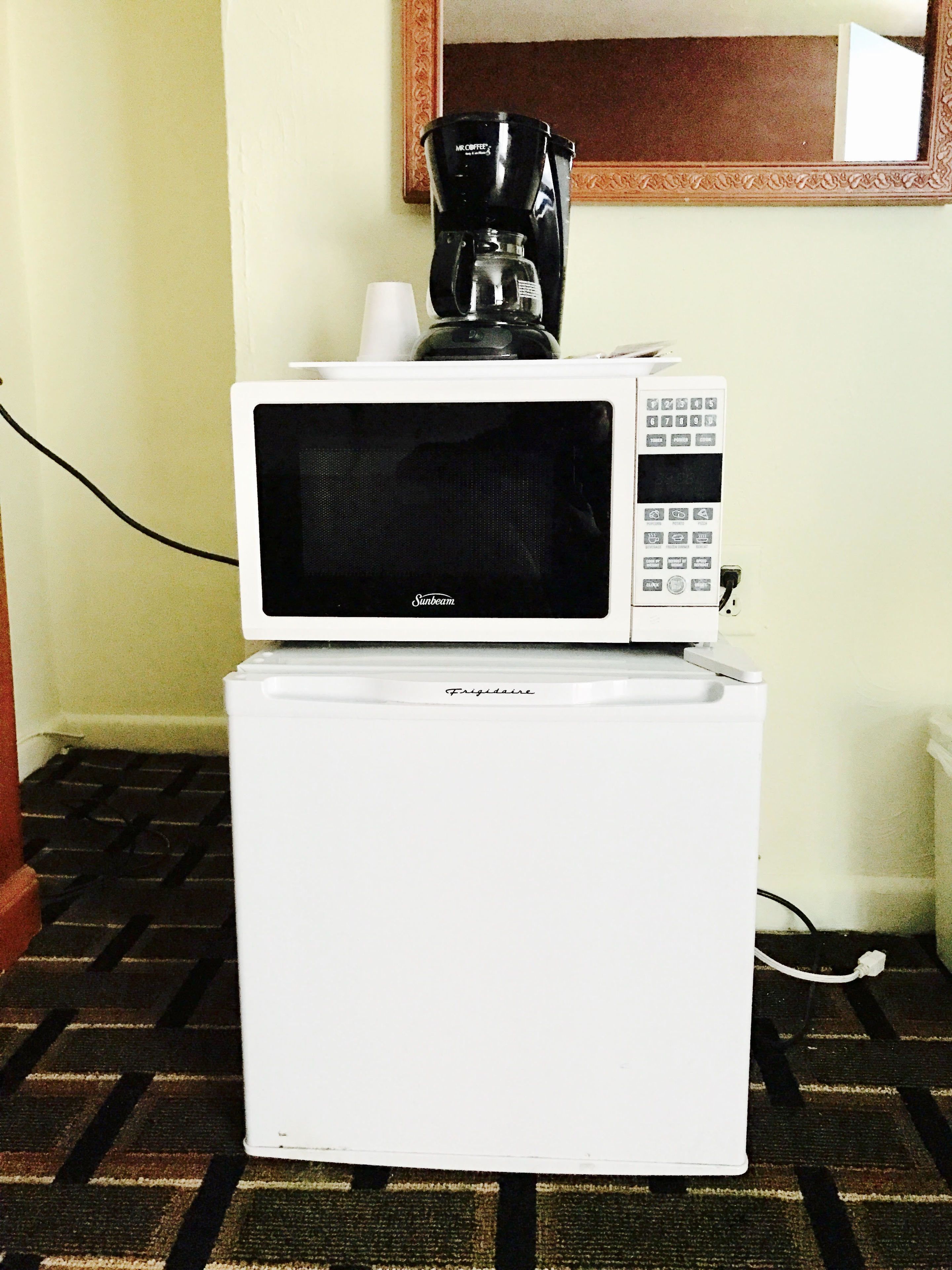 A white refrigerator with a microwave on top, a coffee maker, and a power cord plugged in.