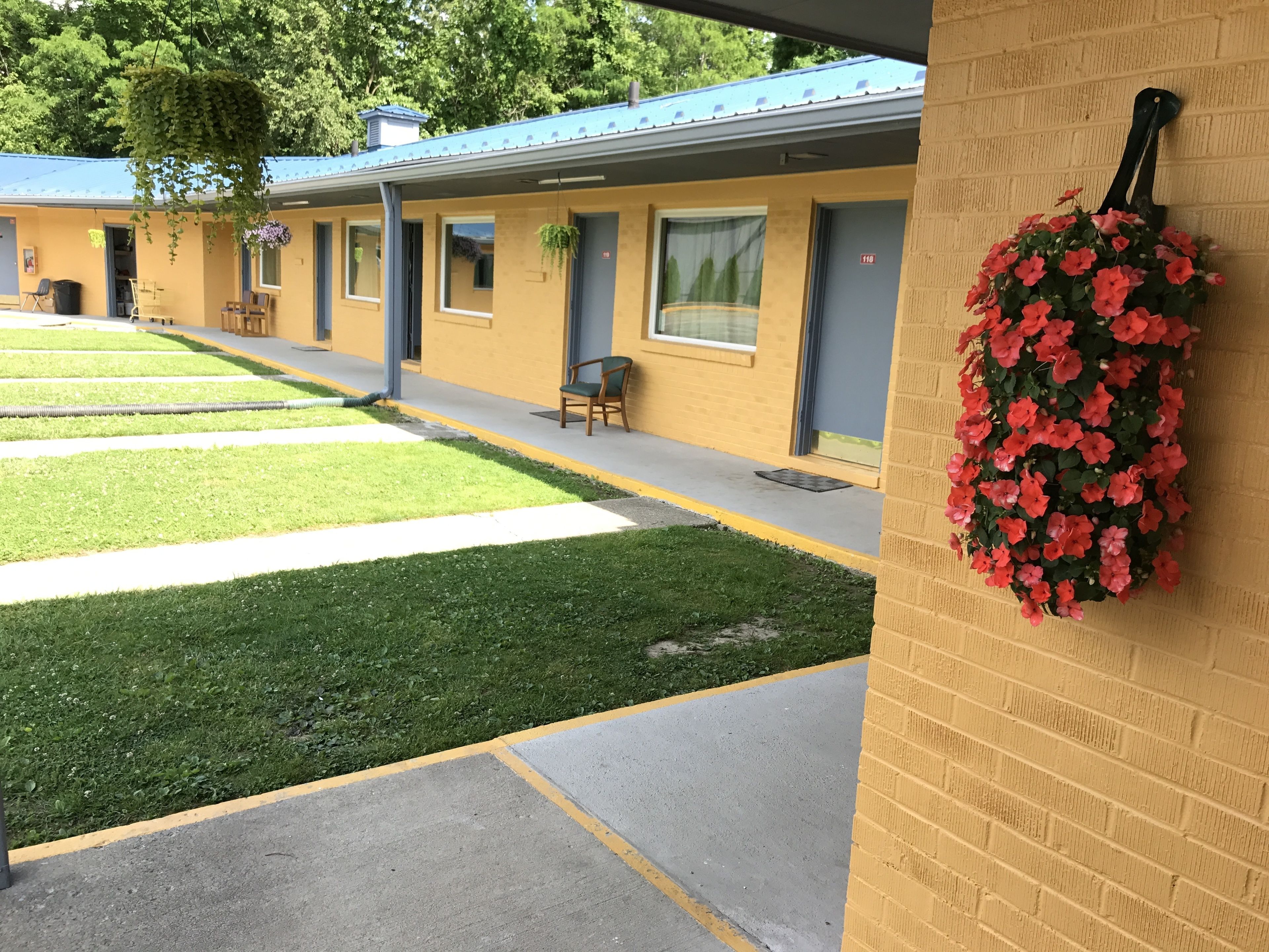 A motel with a yellow exterior, a covered walkway, and a hanging flower basket.