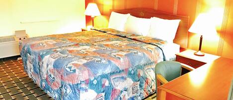 A hotel room with a large bed, two bedside lamps, a wooden headboard, a small table, and a chair.