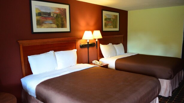 A hotel room with two beds, a wooden headboard, a nightstand with a lamp, and two framed pictures on the wall. - Greystone Motel (Hillsboro)