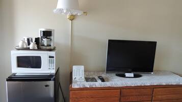 A kitchenette with a microwave, coffee maker, and a flat-screen TV on a wooden dresser.