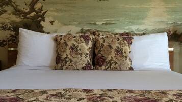 A bed with floral bedding, two white pillows, and a painting of a tree and landscape on the wall behind.