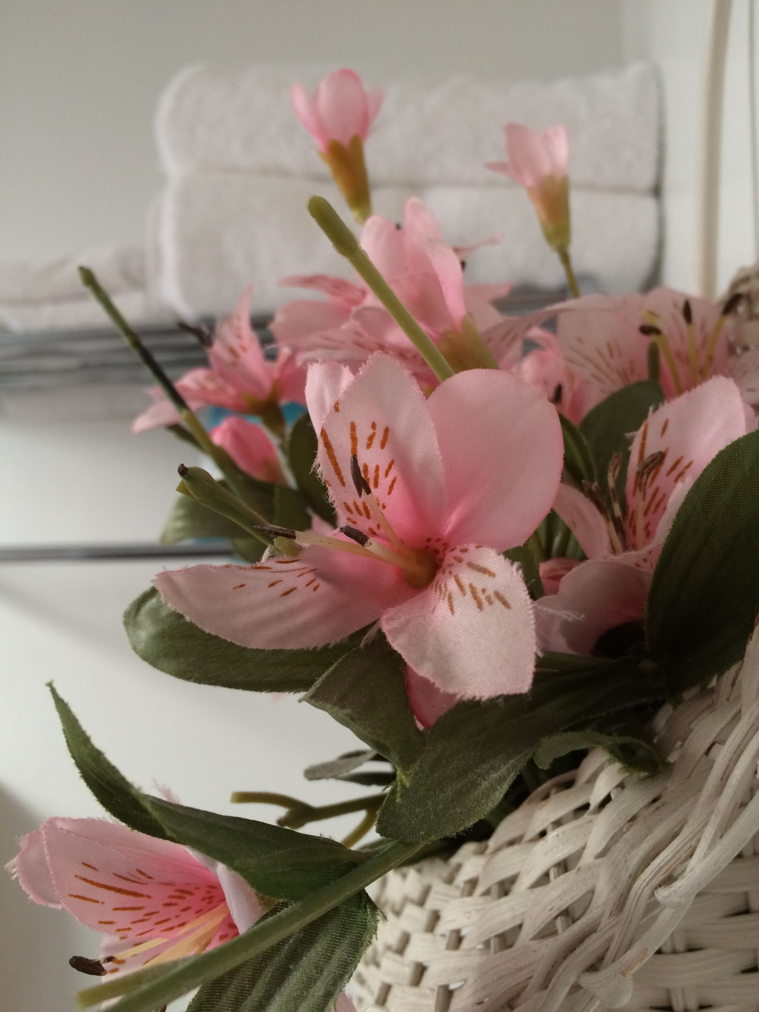 A close-up of a wicker basket containing pink artificial flowers with green leaves.