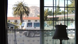 Ein Fenster mit Spitze, eine Lampe und der Blick auf einen weißen Lieferwagen sowie ein Gebäude mit rotem Dach.