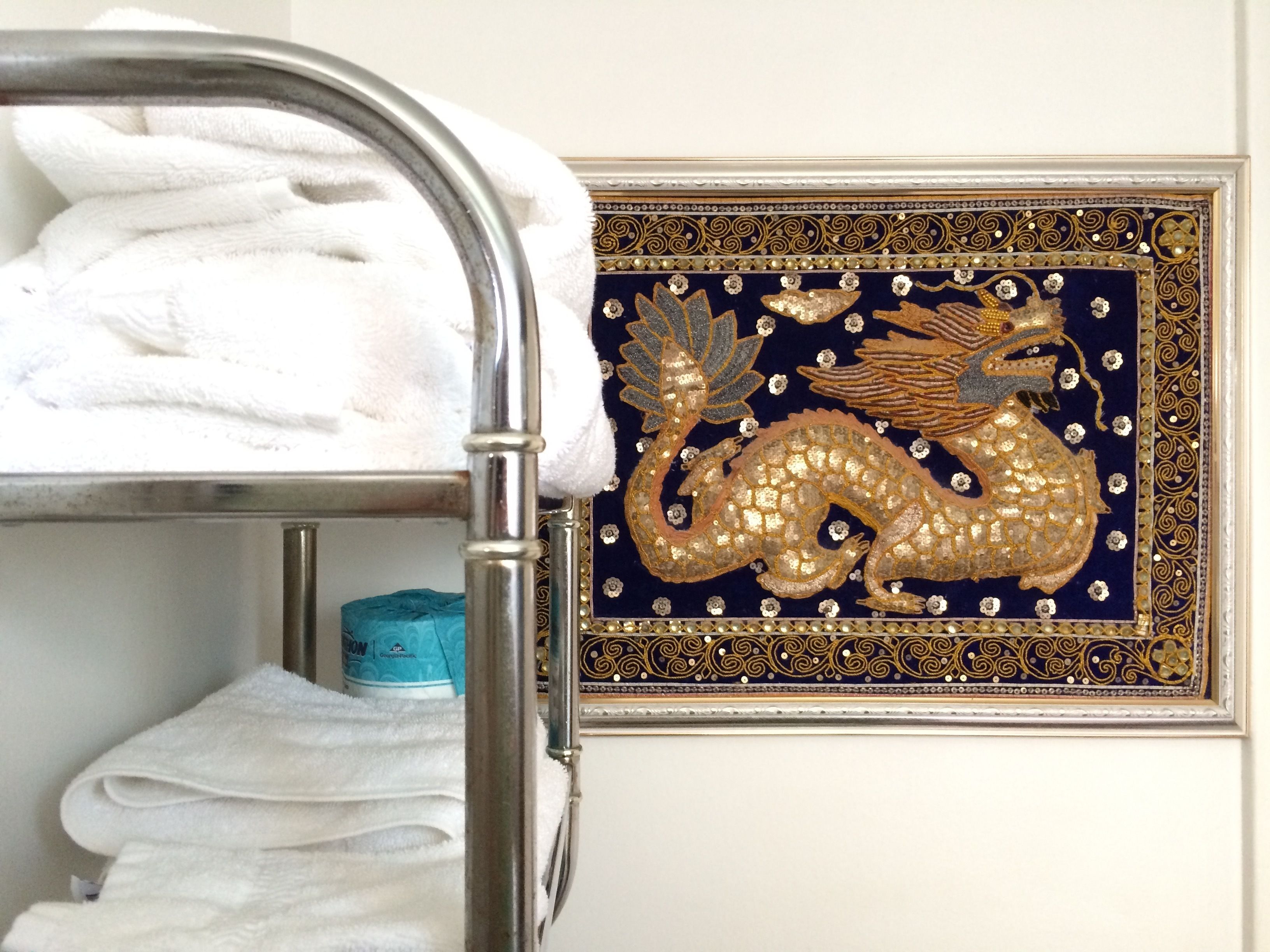 Una cama litera de metal con toallas blancas y un cuadro con un dragón dorado en la pared.