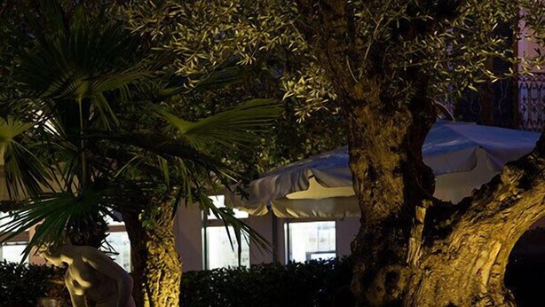 Una estatua de una figura sentada en un jardín con árboles y una zona cubierta.
