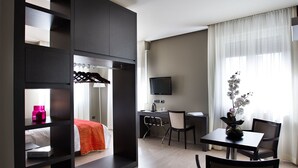 Habitación de hotel con cama, escritorio, silla, televisión y ventana con cortinas.