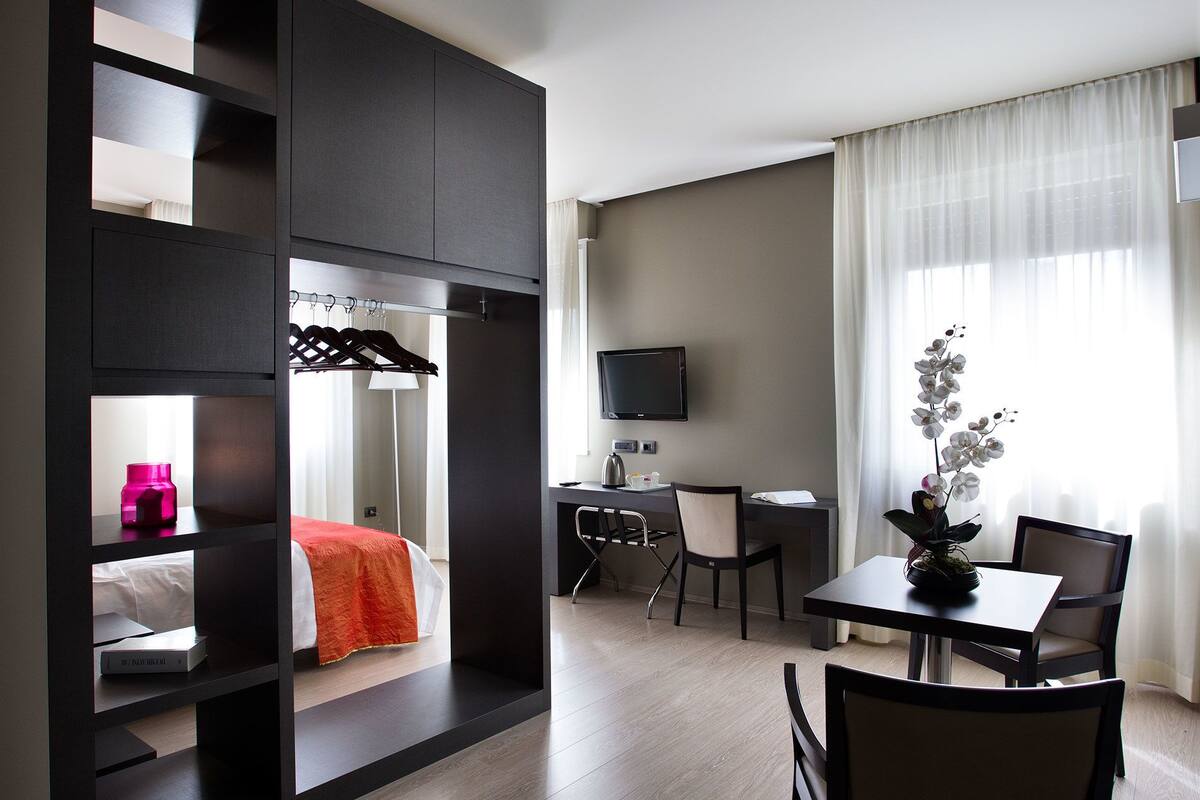 A hotel room with a bed, a desk with a chair, a television, and a window with curtains.