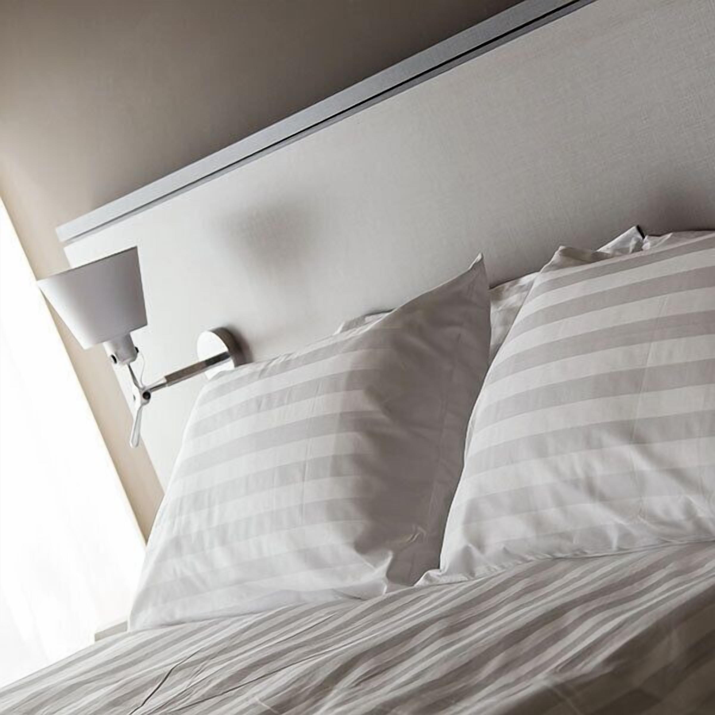 Una cama bien tendida con almohadas a rayas y un cabecero blanco.