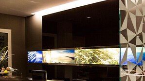 Un espacio de oficina moderno con dos monitores grandes en una pared, un mostrador de recepción y un separador de vidrio con diseño.