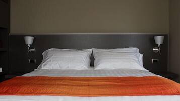 Un lit bien fait, avec une literie blanche et orange, flanqué de deux lampes fixées au mur.